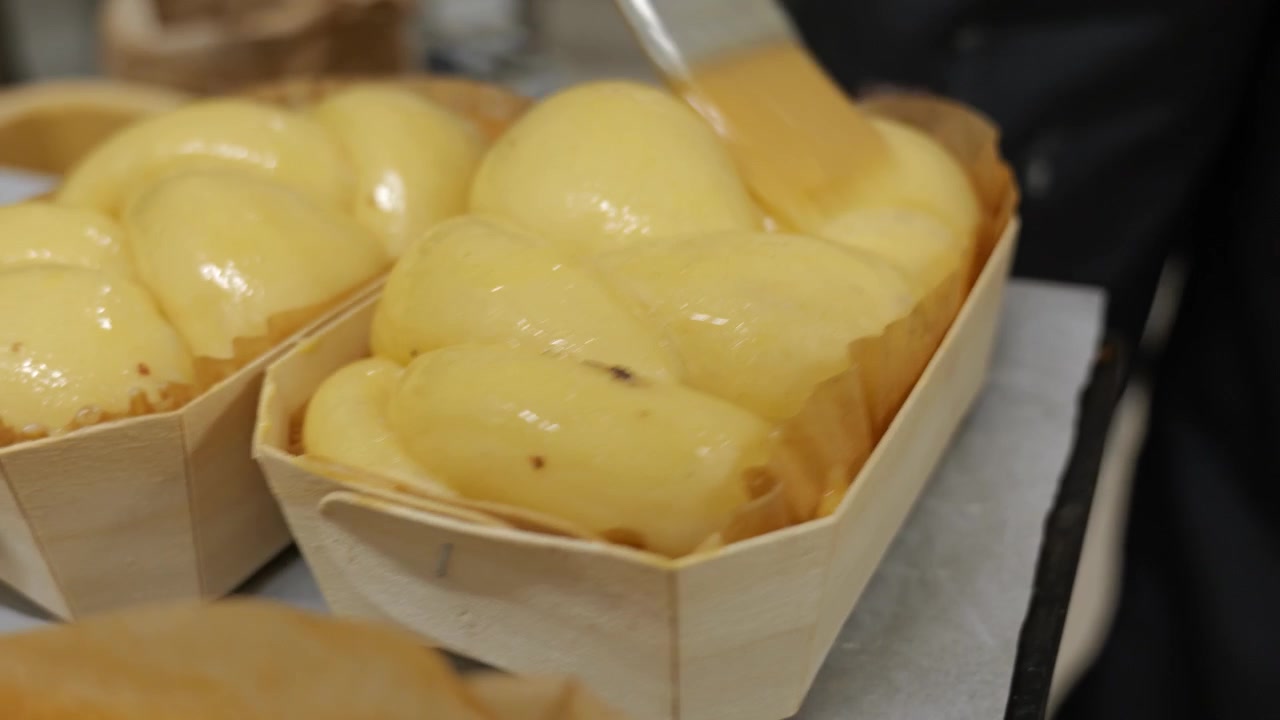 Close up of A baker glazes golden braided brioche loaves with egg wash before baking
