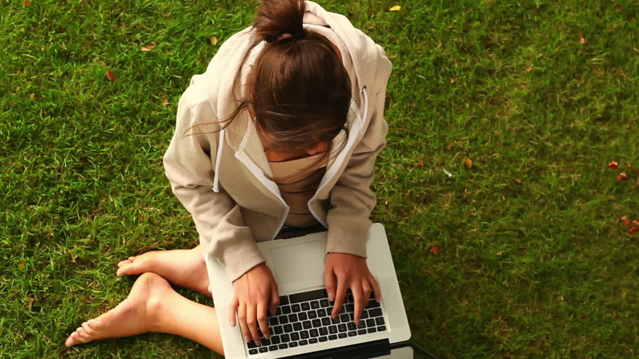 Student working with laptop sitting on lawn