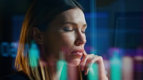 una mujer de primer plano analizando datos del mercado de valores en el reflejo de un holograma en una oficina oscura.