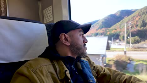 south asian man gazes out train window at picturesque landscape during solo travel journey.