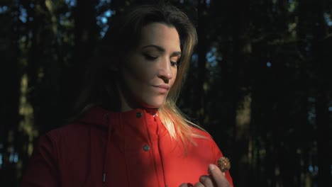 mujer de pie en la luz del sol del bosque sosteniendo el cono de pino