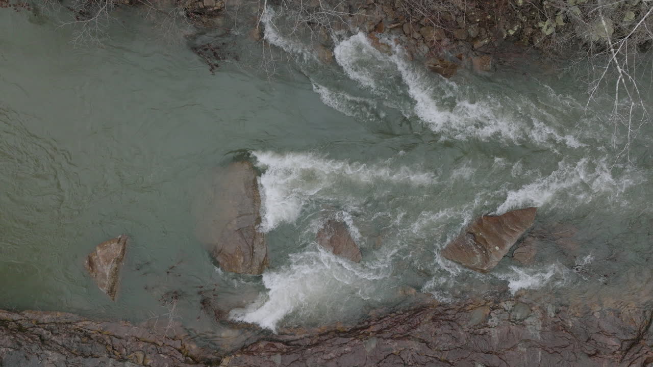 Ripresa aerea con drone dall'alto verso il basso dell'acqua che scorre impetuosa tra le rocce nel torrente