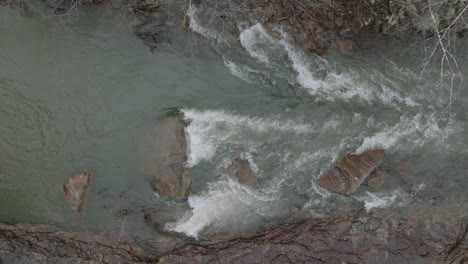 Aerial-top-down-drone-shot-of-water-rushing-past-rocks-in-creek