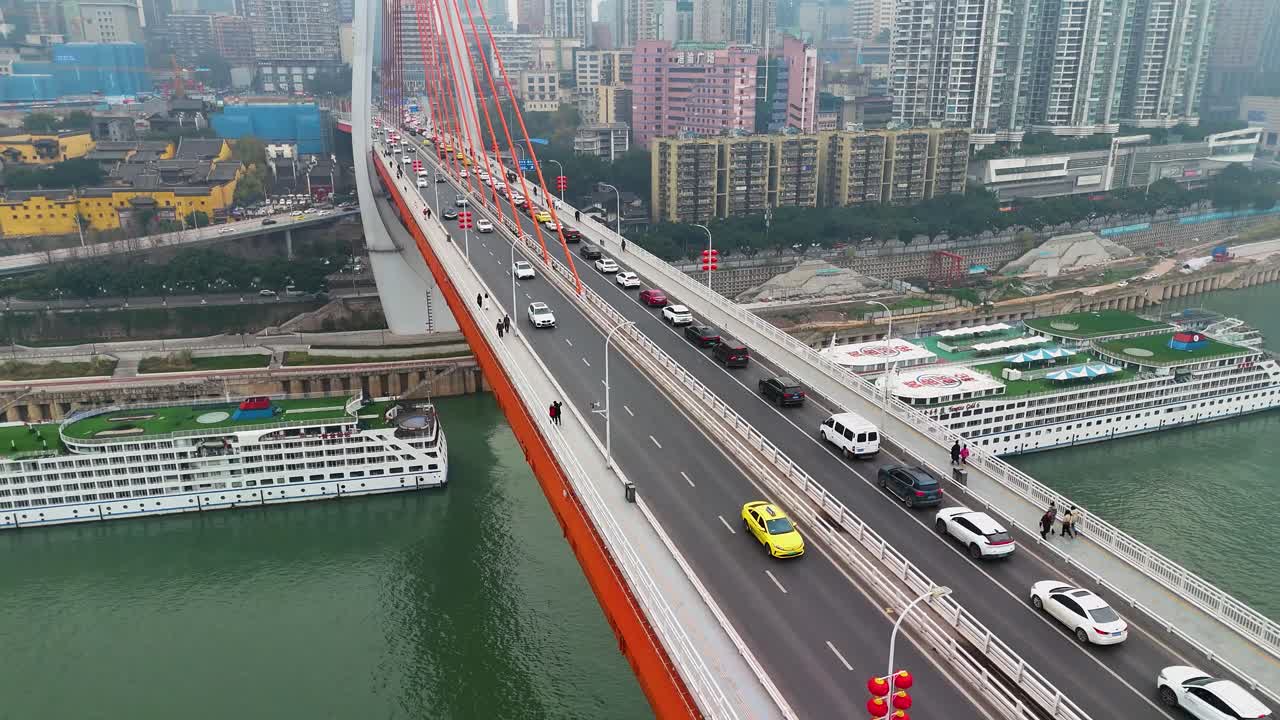 Aerial view of the Dongshuimen Bridge in Chongqing, China, highlighting the flowing traffic and striking orange suspension cables. The dynamic energy of busy bridge connects various parts of the city.