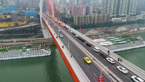 aerial view of the dongshuimen bridge in chongqing, china, highlighting the flowing traffic and striking orange suspension cables. the dynamic energy of busy bridge connects various parts of the city.