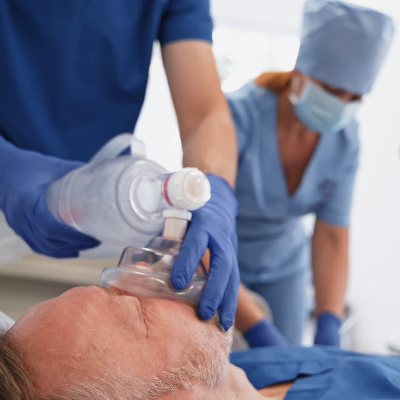 Saving life to unconscious man. Doctor puts an oxygen mask to a sick patient in emergency room. Nurse and specialist giving reanimation to a patient. Close-up.