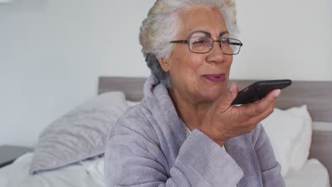 Afroamerikanische-ältere-Frau,-Die-Auf-Dem-Smartphone-Spricht,-Während-Sie-Zu-Hause-Auf-Dem-Bett-Sitzt