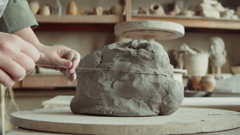 hands of sculptor cutting piece of clay with wire