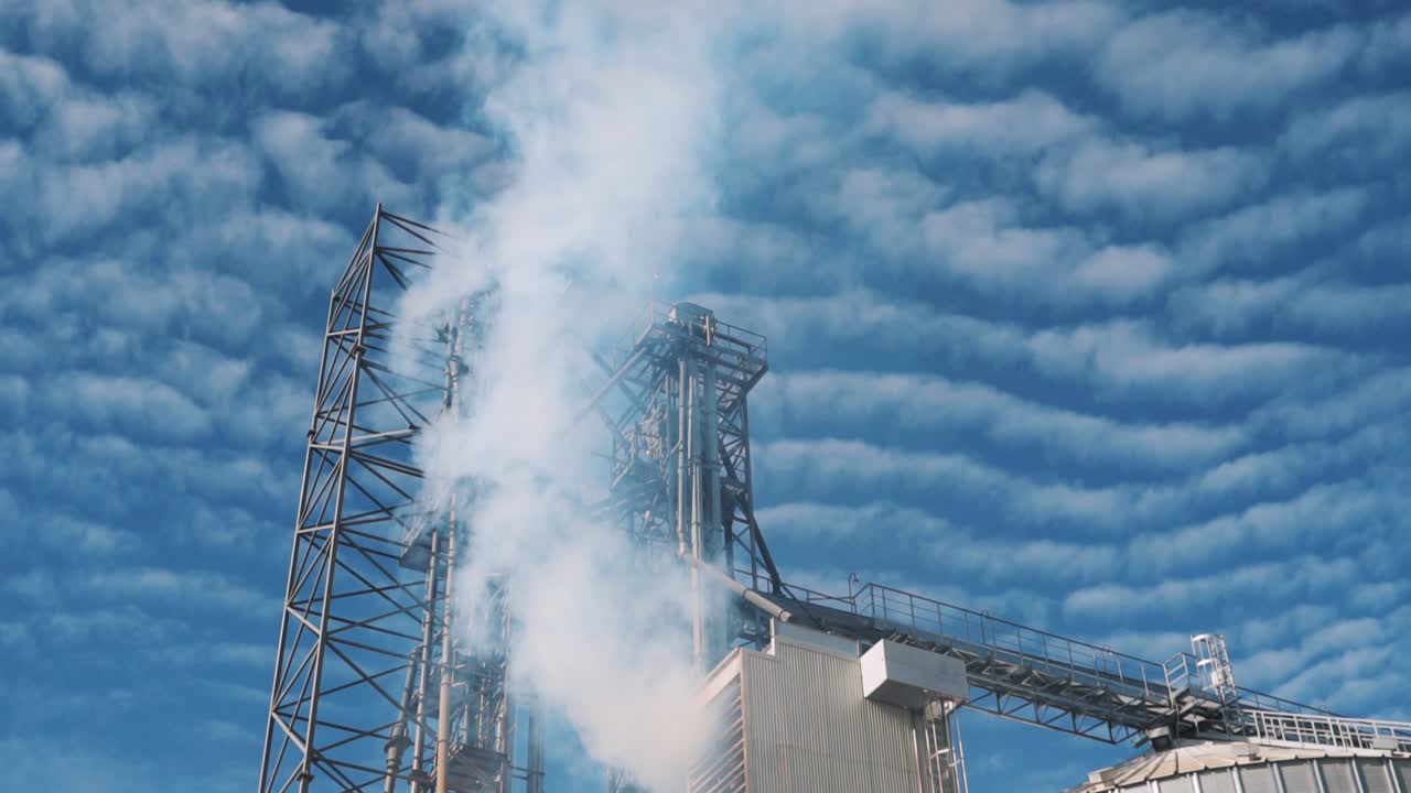 Grain dryer. White smoke from chimneys on the background of the sky with clouds. grain elevator