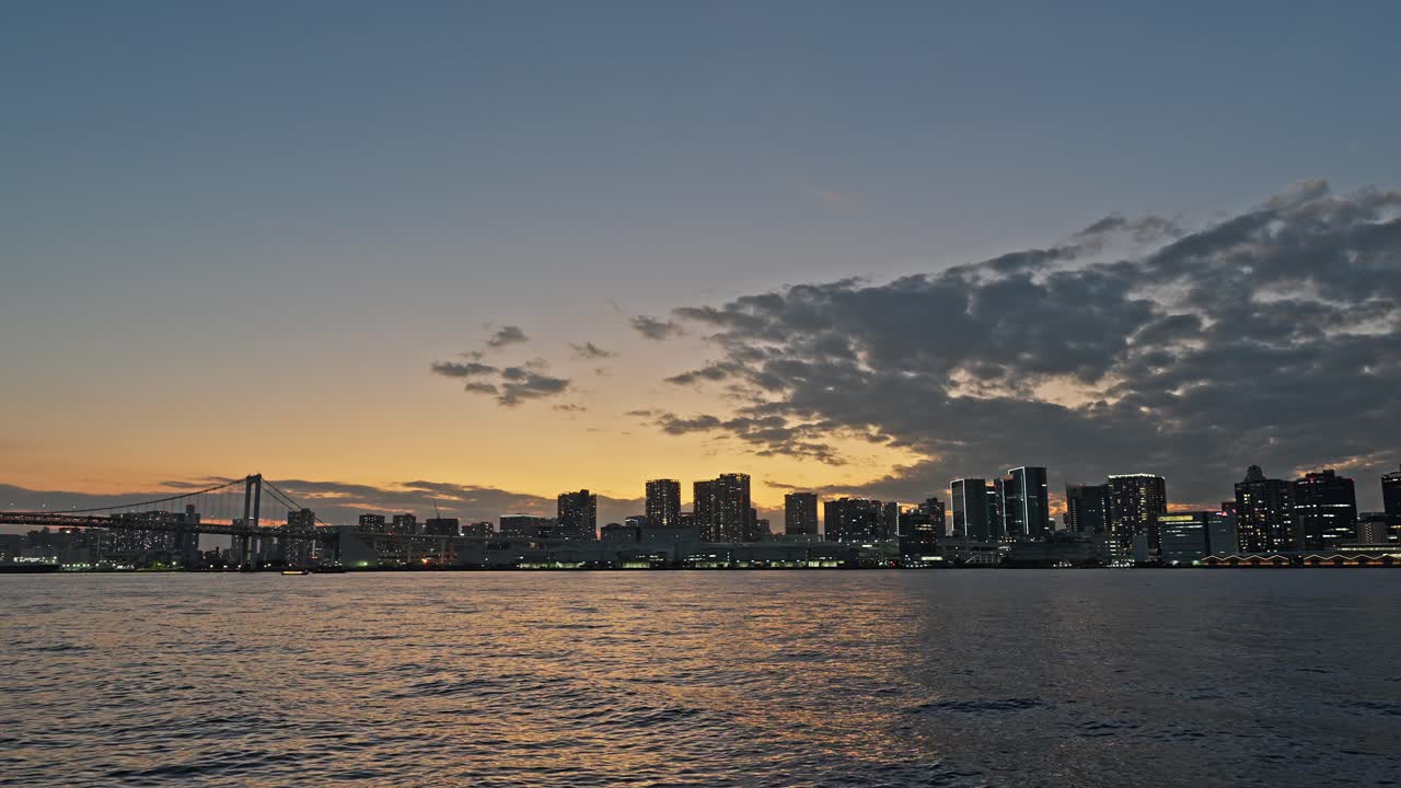 Wide shot of the Tokyo Bay skyline and water at sunset with warm orange and purple colors in the dramatic sky