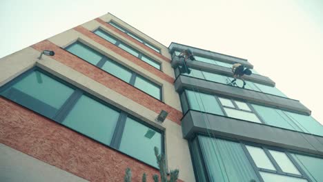 looking up to high altitude climber alpinists cleaning windows on high office building