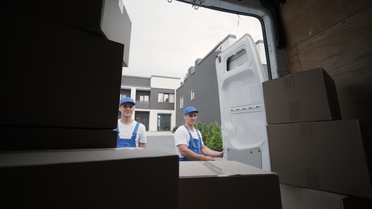 引っ越し会社の2人の若い労働者がミニバスから箱と家具を卸し,顧客の家に