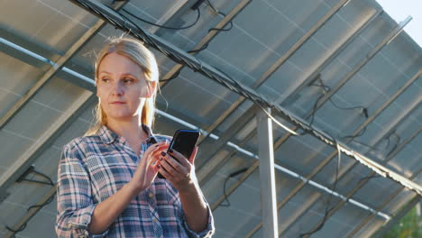 the woman uses a smartphone stands at the inverter under the panels of the house