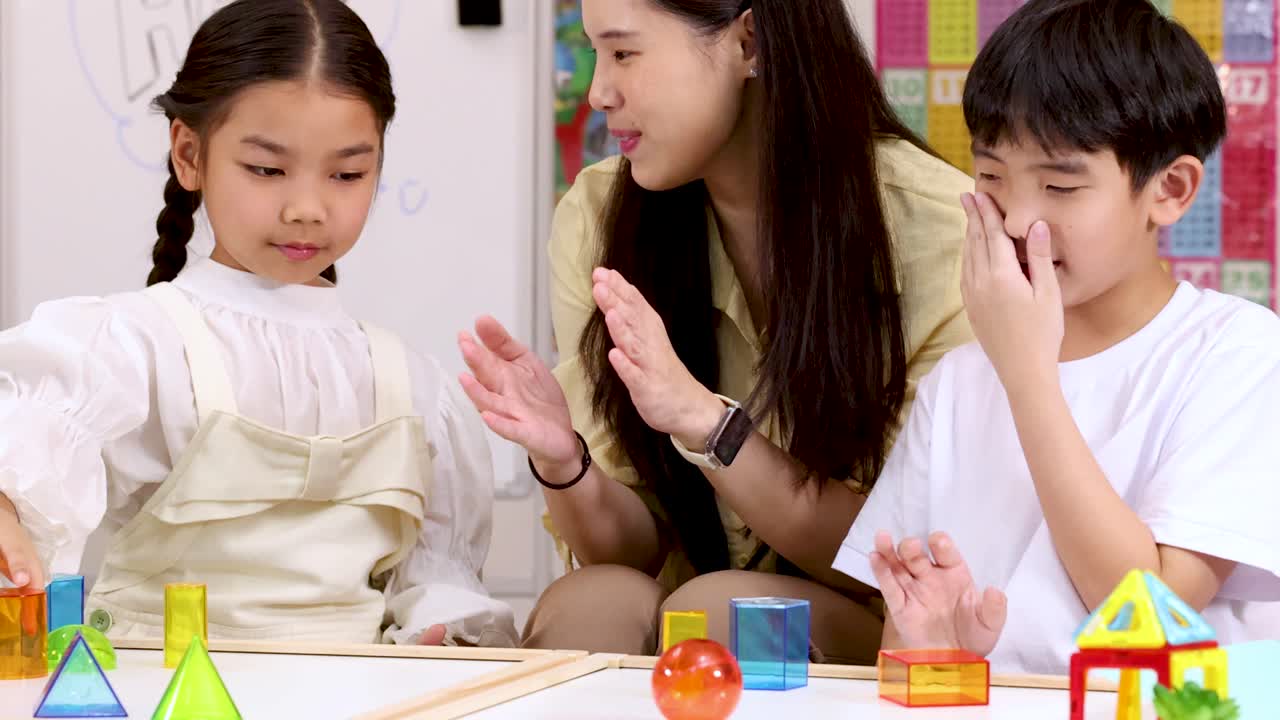 2人の子供と教師が明るい教室で、カラフルなブロックを使って笑顔で触れ合い、学んでいます。