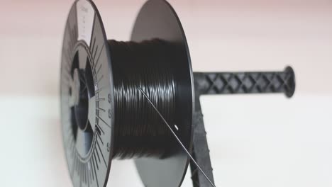 a spool of black 3d printer filament sits on the 3d printer spool holder and winds down while its being printed with