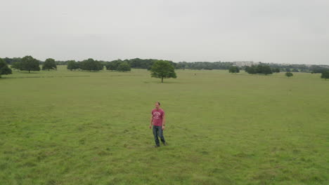 Aerial-shot-of-a-man-walking-in-a-green-open-space,-camera-rotates-round-while-walking