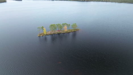 red wooden cabin with autumnal trees in an islet surrounded by lake in sweden