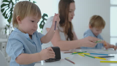 the child sharpens a pencil, and mom and son sitting at the table draw a picture together