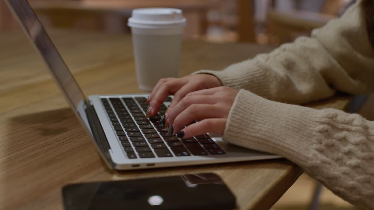 Push in on girls hands typing on laptop keyboard in cafe