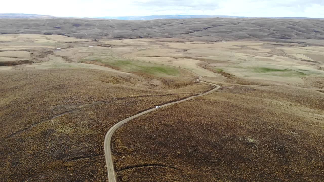 un coche blanco conduce por un lago remoto en una carretera lenta en el medio de otago central.
