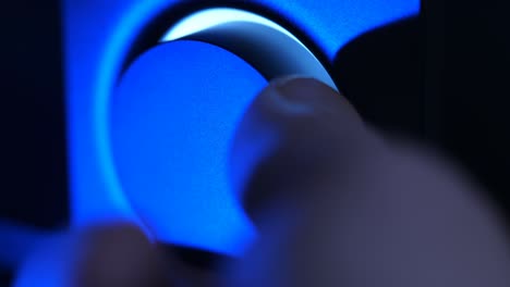 en la oscuridad, la mano gira el control de volumen, iluminado por luz azul