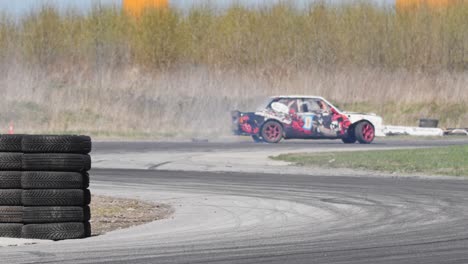 Tiro-A-Cámara-Lenta-De-Un-Coche-A-La-Deriva-En-Una-Pista-De-Carreras-Con-Un-Montón-De-Neumáticos-Y-Giro-S