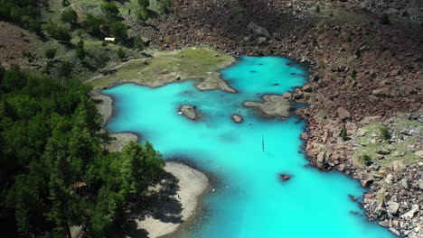 cinematic drone shot of turquoise colored water in the mountains at naltar valley in pakistan, slow revealing aerial shot