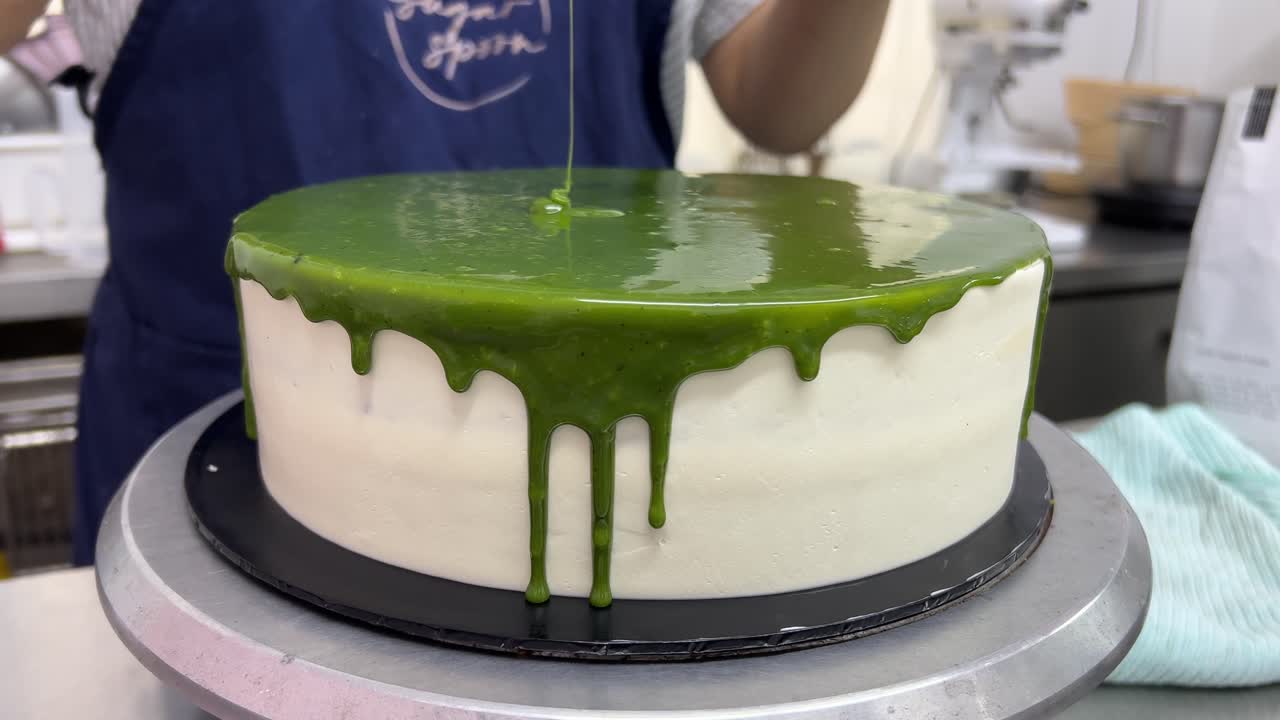 Far girare il piatto girevole per levigare la glassa a specchio al cioccolato matcha, primo piano.