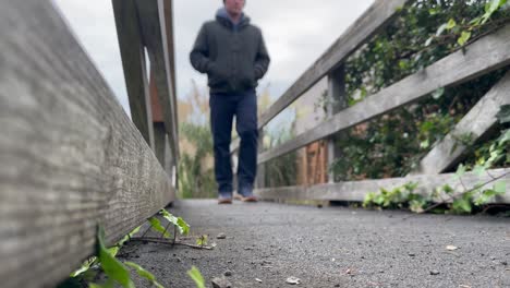 blurry shot of a man walking on footbridge with wooden handrails