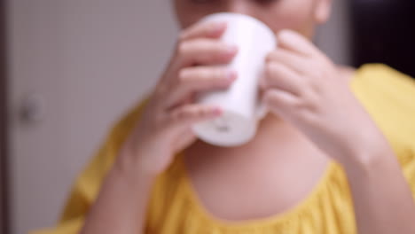 close-up of a woman who is wearing a yellow dress is holding a mug while sipping and drinking some coffee