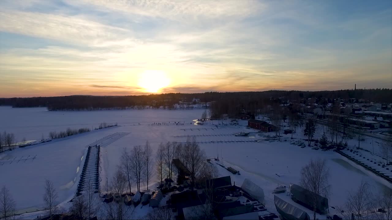 People are playing on frozen lake in Nokia town, Finland. Drone shot of boat harbour, snowy land and housing area.