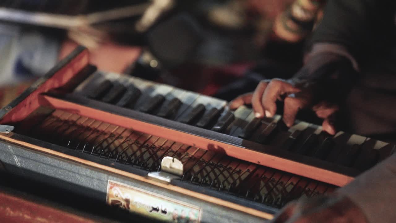 Primo piano di mani che suonano un armonium in Sindh, Pakistan, che cattura una performance di musica folk tradizionale con luce calda e profondità di campo ridotta