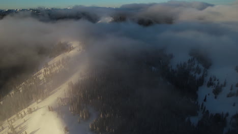 Vista-Aérea-Del-Prístino-Paisaje-Montañoso-En-La-Mañana-De-Invierno,-Volando-Sobre-Nubes-Claras-Y-Bosques-De-Pinos