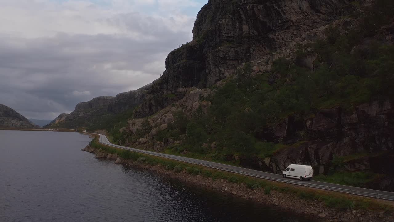 A van driving along a scenic Norwegian road surrounded by dramatic mountains and water