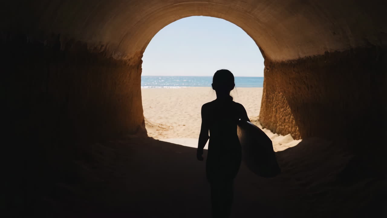 Surfer walking through a tunnel towards the beach