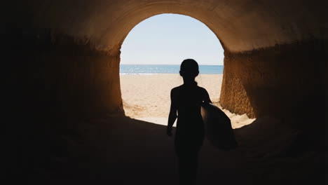 surfer walking through a tunnel towards the beach