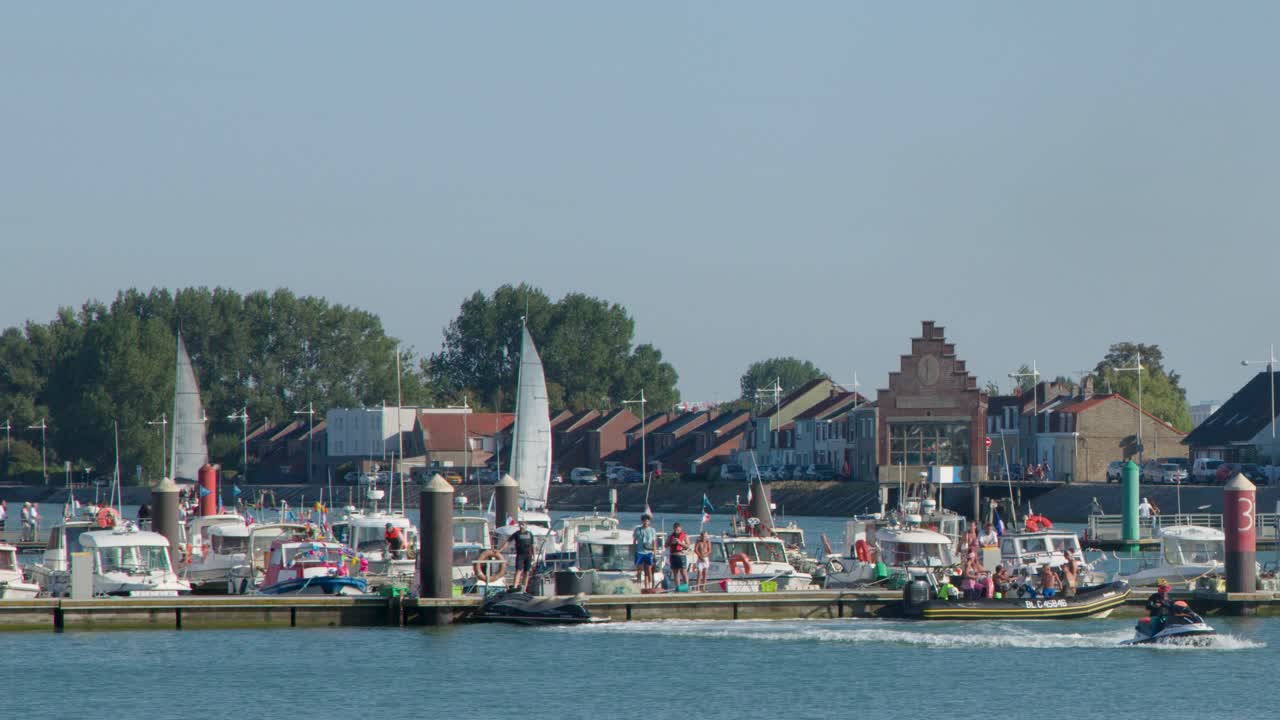 Jet ski moves across marina, boats docked, people on pier, sunny summer day, steady camera