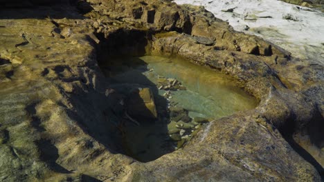 small rock pool during golden hour cut out by years of erosion, ancient rock