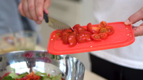 chef putting the fresh and chopped red tomatoes into a stainless bowl for vegetable salad. close up shot