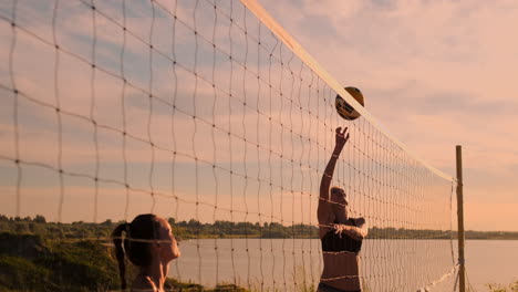 SLOW-MOTION-LOW-ANGLE-CLOSE-UP-SUN-FLARE:-Athletic-girl-playing-beach-volleyball-jumps-in-the-air-and-strikes-the-ball-over-the-net-on-a-beautiful-summer-evening.-Caucasian-woman-score-a-point.