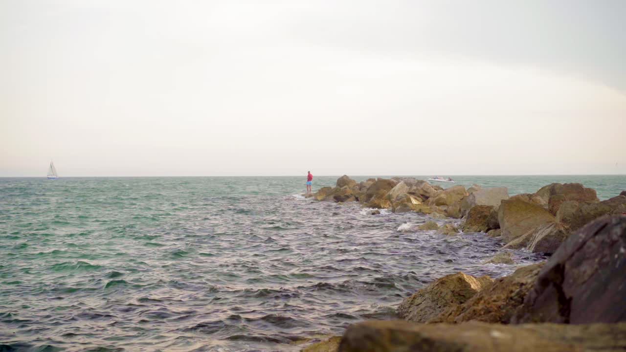 바위 위에 서서 험난한 바다에서 낚싯대를 던지는 어부