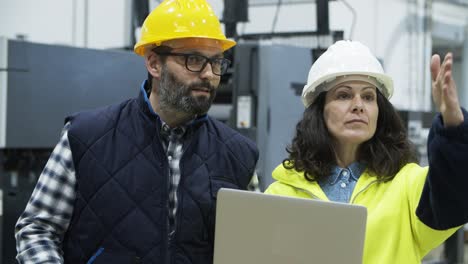 ingenieros enfocados discutiendo el trabajo mientras están de pie con la computadora portátil