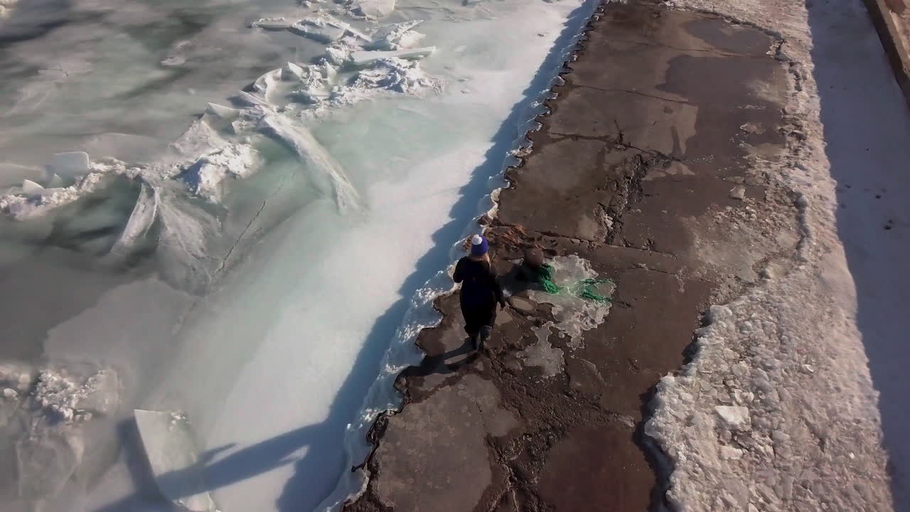 푸른 겨울 모자를 쓴 여자가 얼어붙은 얼음 호수 옆 선착장을 따라 걷고 있다