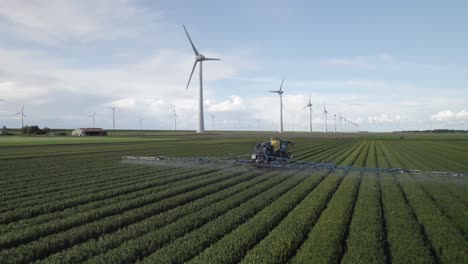 tractor sprays crops in open fields as wind turbines rotate in the background, illustrating a blend of old and new technologies.
