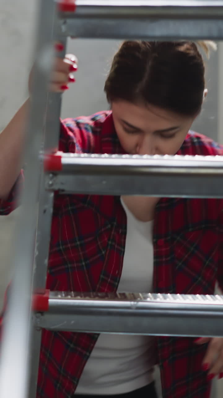 Woman drops down brush climbing on step ladder in living room. Lady prepares to apply paint on walls in apartment. DIY domestic renovation process