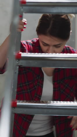 woman drops down brush climbing on step ladder in living room. lady prepares to apply paint on walls in apartment. diy domestic renovation process