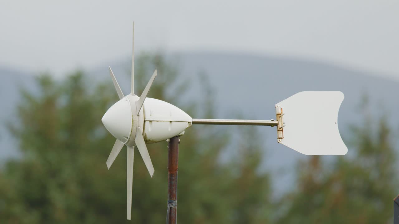 A compact wind turbine spins steadily in a rural landscape, with overcast daylight and gentle camera stability highlighting renewable energy in action