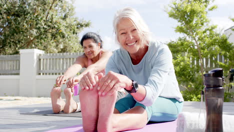 two happy diverse senior women stretching and smiling in sunny garden, slow motion
