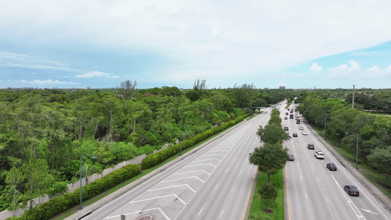 “Welcome to Naples” sign near palm trees and traffic along a highway in Naples, Florida. Includes a Tree City USA recognition sign on the roadside with cars passing. Aerial.