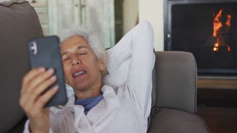 Senior-mixed-race-woman-lying-on-sofa-using-smartphone